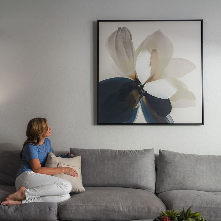 Minimalist living room with a large abstract flower painting on the wall, a wooden console with decorative vases, books, and a beige sofa with a light pillow.