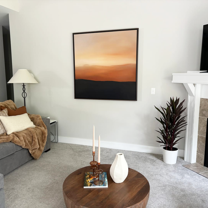 A cozy living room with a gray sofa, brown throw blanket, floor lamp, round wooden coffee table with candles and a vase, potted plant, and Tranquil Vista Abstract Canvas Art on a light gray wall—perfect for stylish decor.