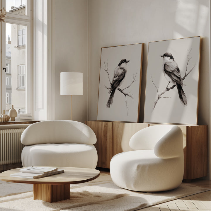 A modern living room features the Still Perch Set of 2 white, rounded armchairs, a low wooden coffee table, and neutral-toned bird art prints by the sideboard. Sunlight through tall windows completes the serene Nordic Park vibe.