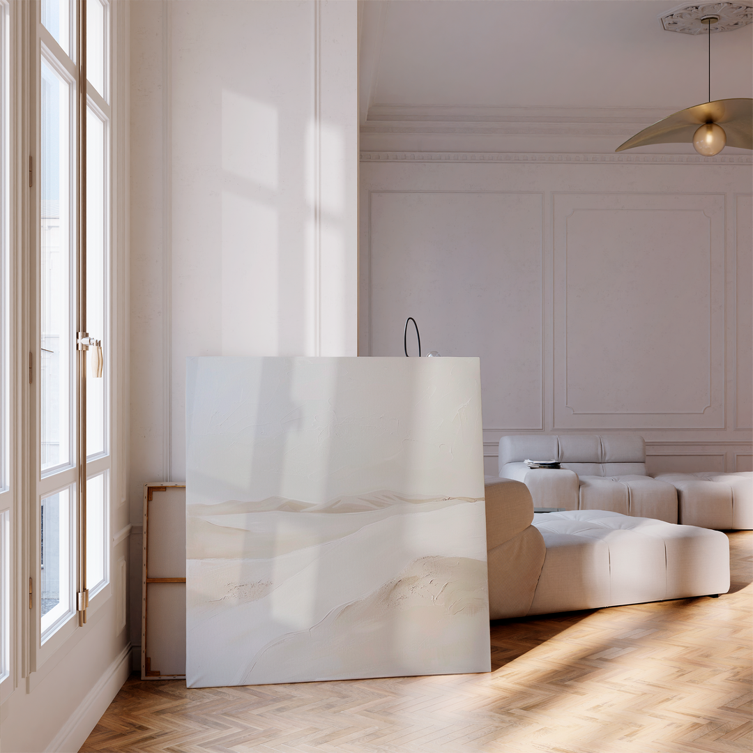 A minimalist living room with light walls, parquet floors, a large white sectional sofa, and the Misty Vale Abstract Canvas Art in neutral tones leaning near tall windows—perfect for refined living room decor.