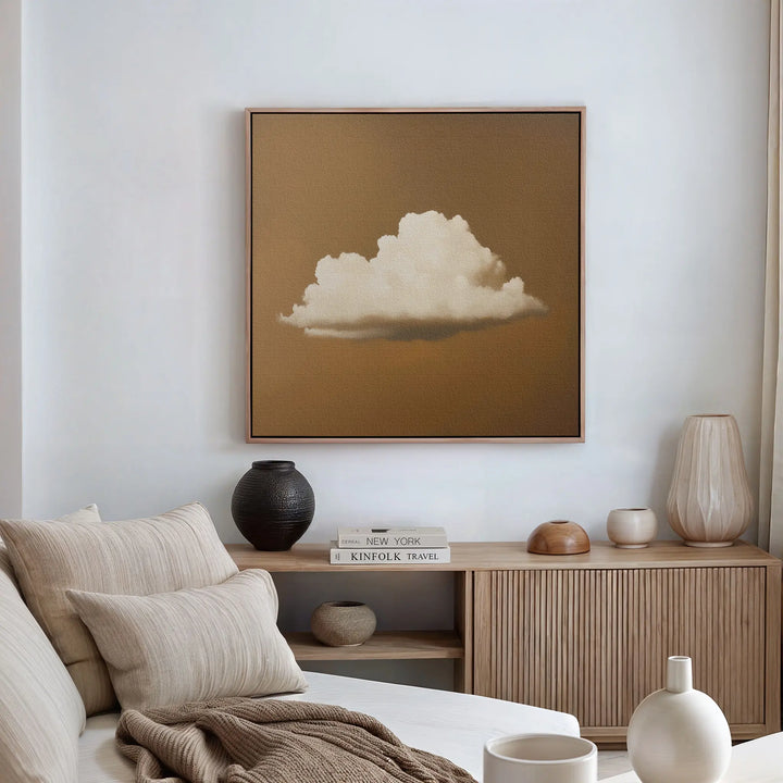 A minimalist living room features a beige couch with striped cushions, a light wood sideboard with vases and books, and modern wall art—Amber Sky Cloud Canvas Art, a framed painting of a white cloud on a brown background—above.