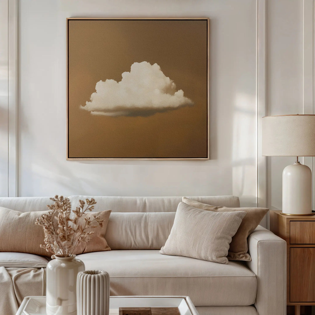 A neutral-toned living room features a white sofa, beige pillows, and a wooden side table with a lamp. Above the sofa hangs the Amber Sky Cloud Canvas Art—a minimalist painting of a white cloud on a brown background.