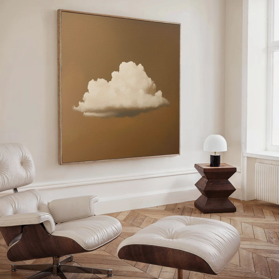 A minimalist living room with a white lounge chair and ottoman, wood floors, a geometric wood side table with a small lamp, and the Amber Sky Cloud Canvas Art featuring a white cloud on brown hanging on the wall.