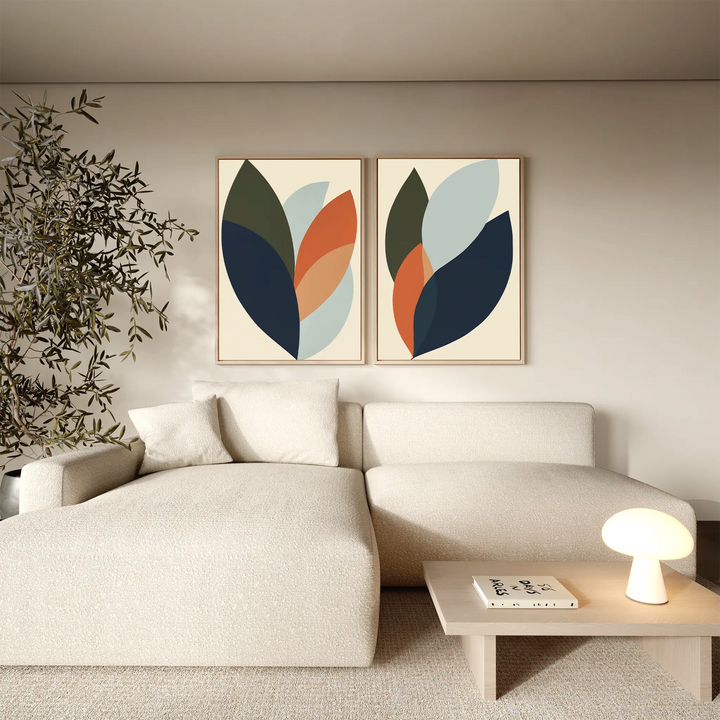 A modern living room featuring a cream sectional sofa, light wood coffee table with magazines and lamp, an indoor plant, and the Autumn Layers Set of 2—striking leaf-themed wall art that enhances the room’s decor.