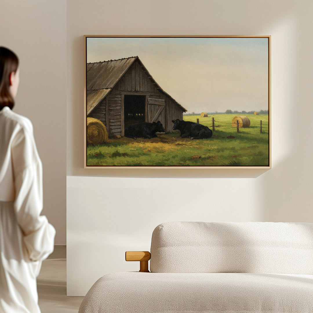 A person in white admires the Barnside Rest Canvas Art, featuring cows and a barn, displayed above a beige sofa and adding charm and warmth to the modern minimal living room.