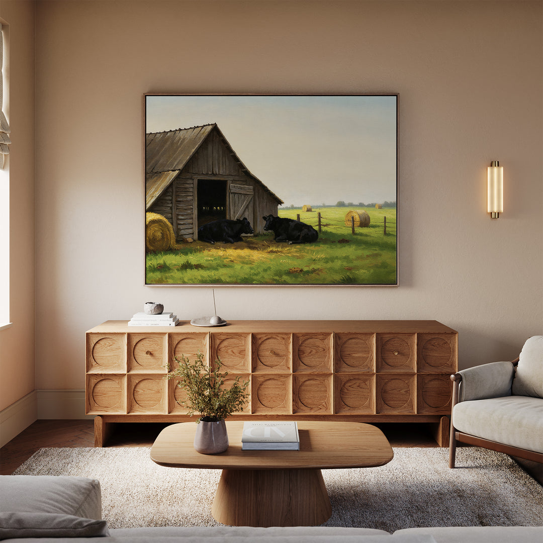 A cozy living room with a wooden sideboard, coffee table, and beige sofas. Above the sideboard hangs the Barnside Rest Canvas Art, depicting a barn scene with cows and hay bales in a green field.