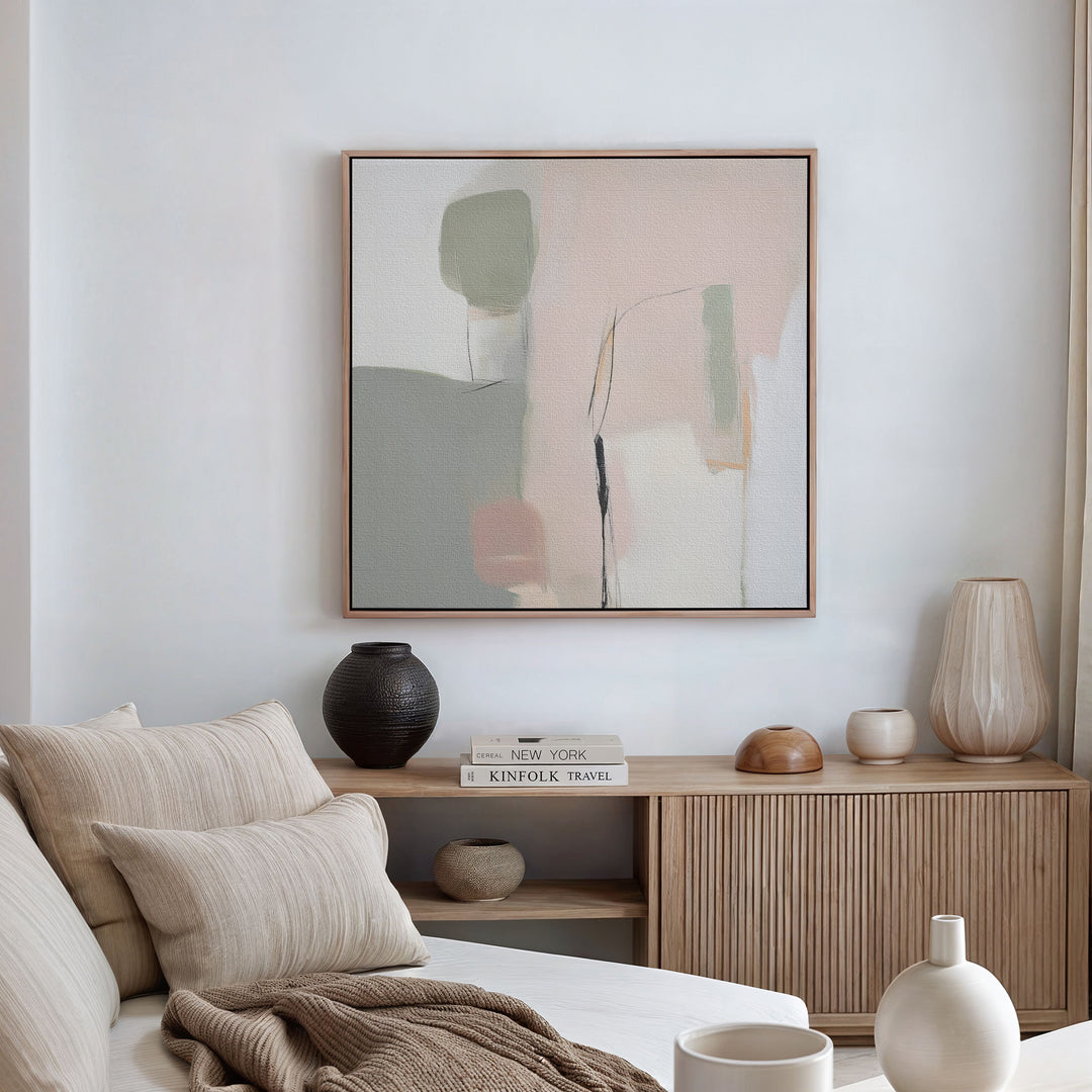 A modern, minimalist living room in neutral tones features a beige sofa with cushions, a wooden sideboard with vases and books, and the Blushed Horizon Canvas Art—an abstract piece in green, pink, and beige—hanging on the wall.