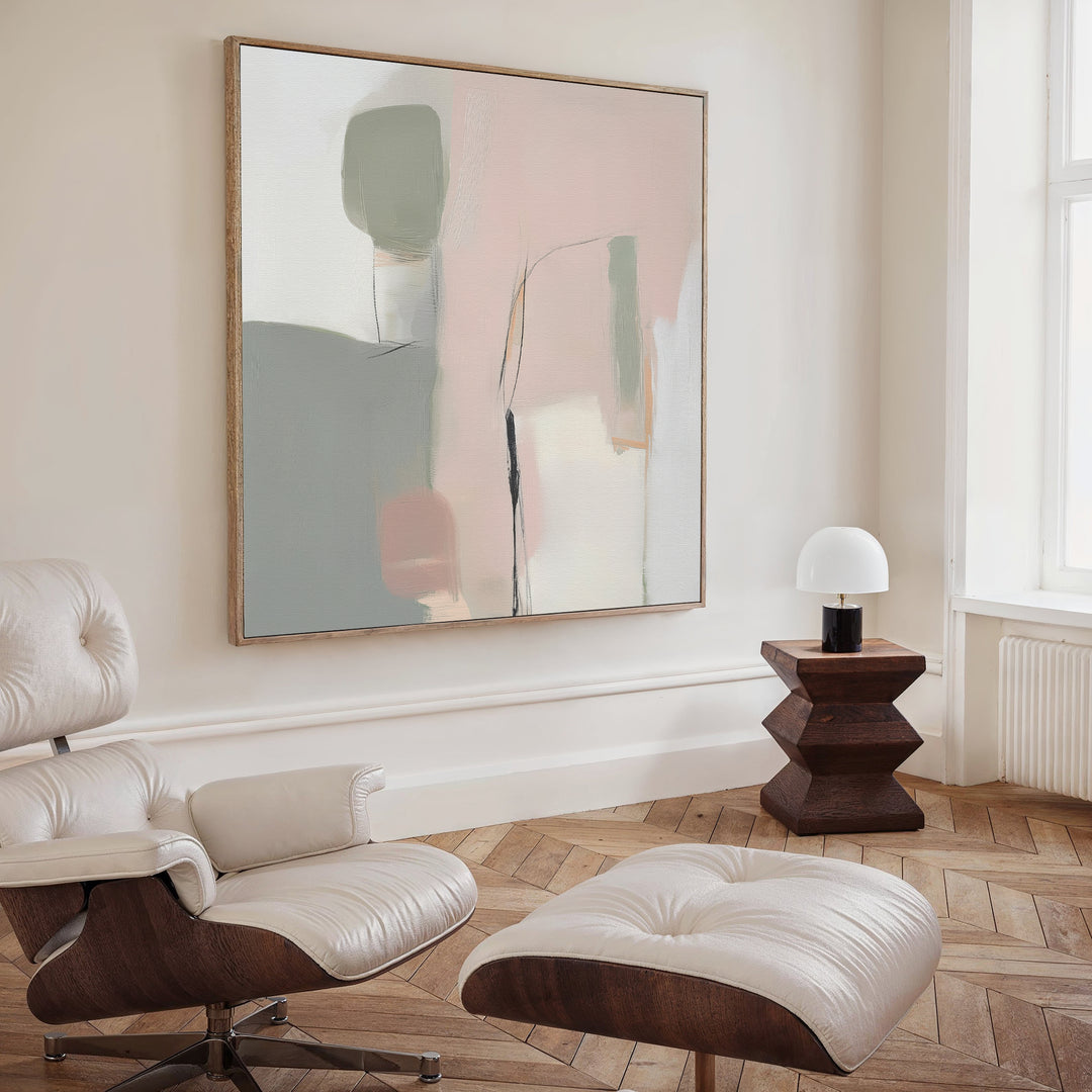 A modern minimalist living room features a white leather lounge chair and ottoman, wooden side table with a white lamp, Blushed Horizon Canvas Art on the wall, herringbone wood floors, and a large window.