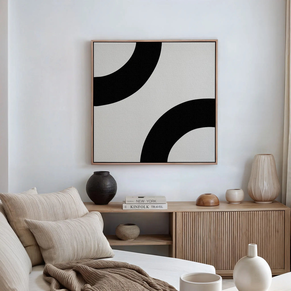 A minimalist living room with a beige sofa, striped cushions, a wooden sideboard topped with books and decorative vases, and the Bold Orbit Canvas Art framed on the wall enhances the modern interior.