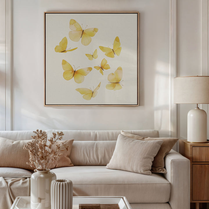 A cozy living room with a beige sofa, neutral pillows, a lamp, and dried flowers in a vase. Above the couch hangs the Butterfly Radiance Canvas Art featuring yellow butterflies, enhancing the warm and minimalistic decor.