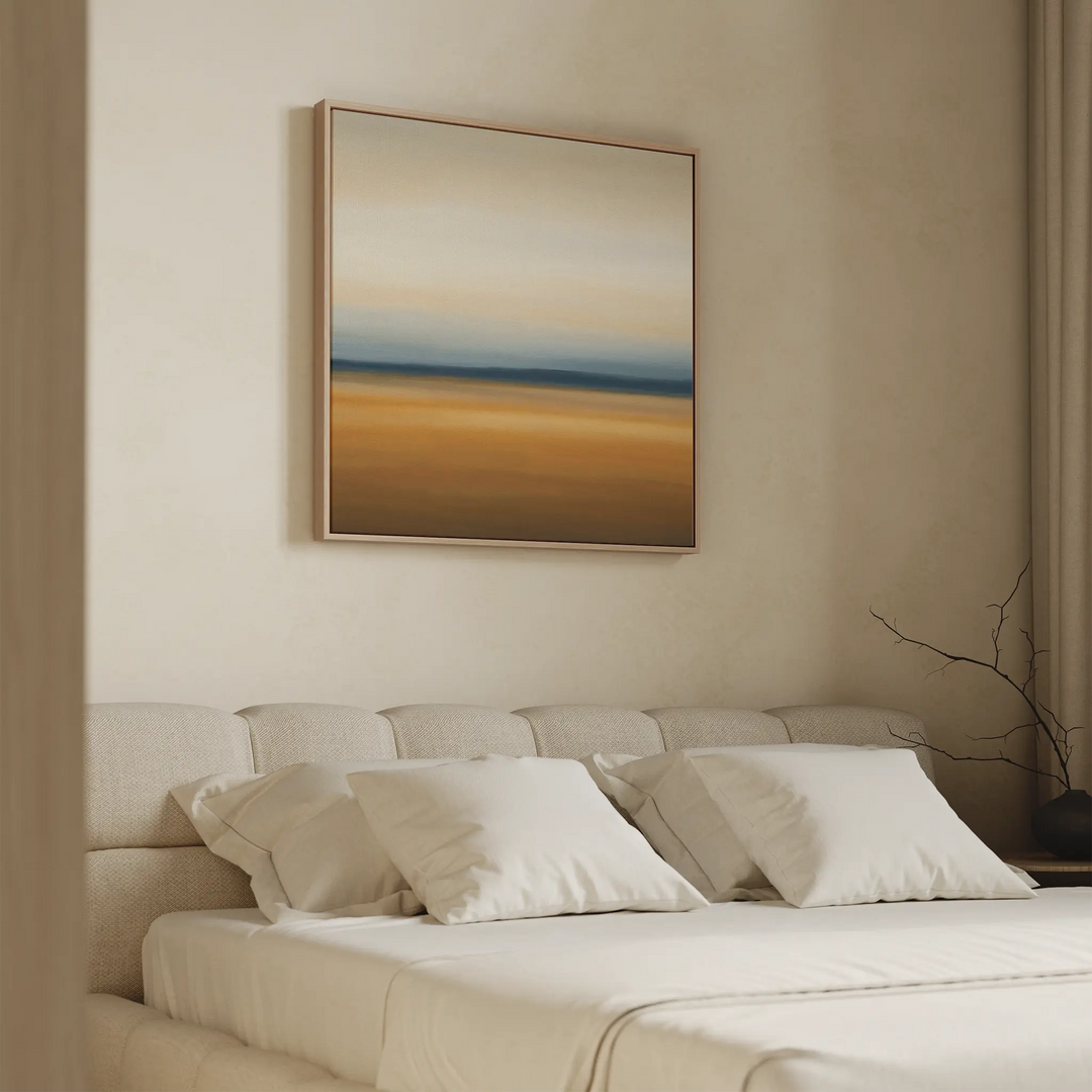 A minimalist bedroom features a beige upholstered bed, white pillows, and a neutral wall adorned with Caramel Plains Canvas Art in earthy tones and soft gradients, creating a calm and serene atmosphere.