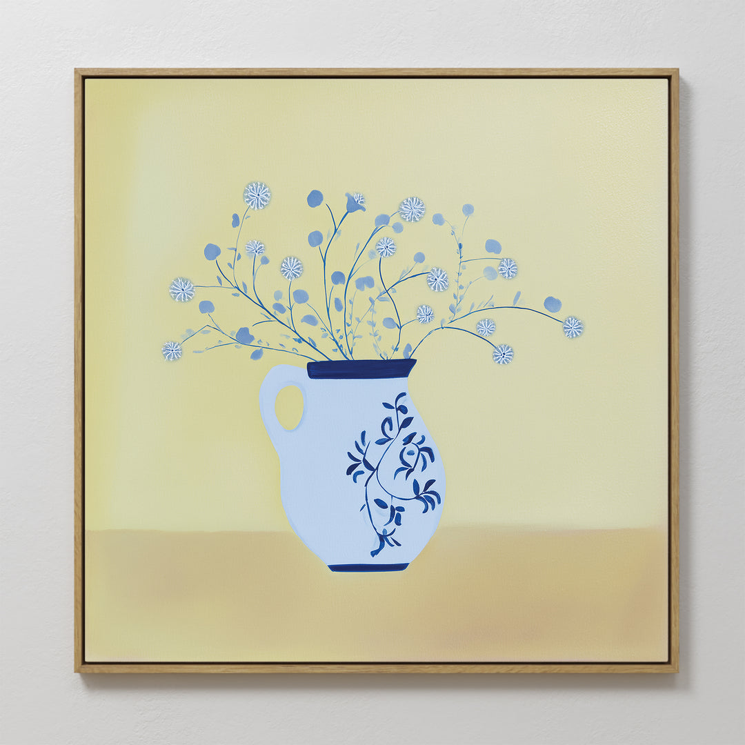 The Cerulean Petals Canvas Art features a blue and white floral vase with delicate round white flowers against a soft yellow background. This minimalist, framed wall decor is perfect for adding elegance to any white wall.