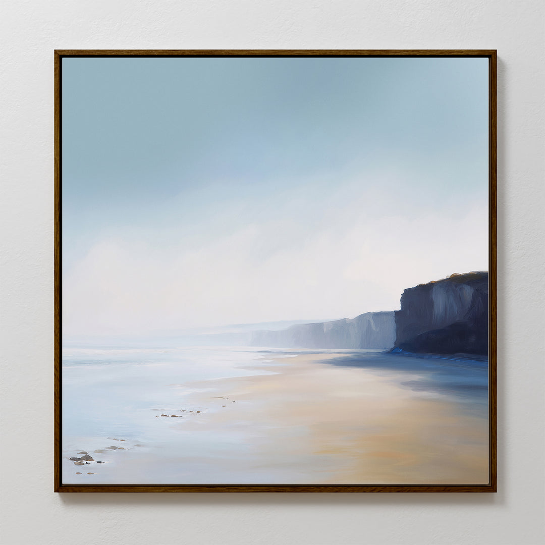 The Cliffside Light Canvas Art features a serene coastal scene with sandy beach, gentle waves, and dramatic cliffs under a hazy blue sky—perfect minimalist wall art for adding calm to any space.
