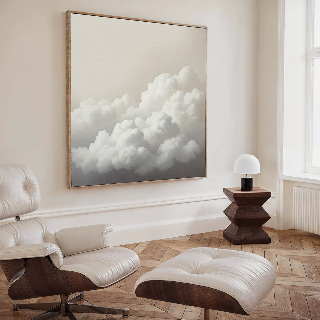 A modern, minimalist living room features Cloud Reverie Canvas Art on the wall, a white leather lounge chair with matching ottoman, a unique wooden side table, and a small lamp. Pale walls and herringbone wood floors complete the serene space.