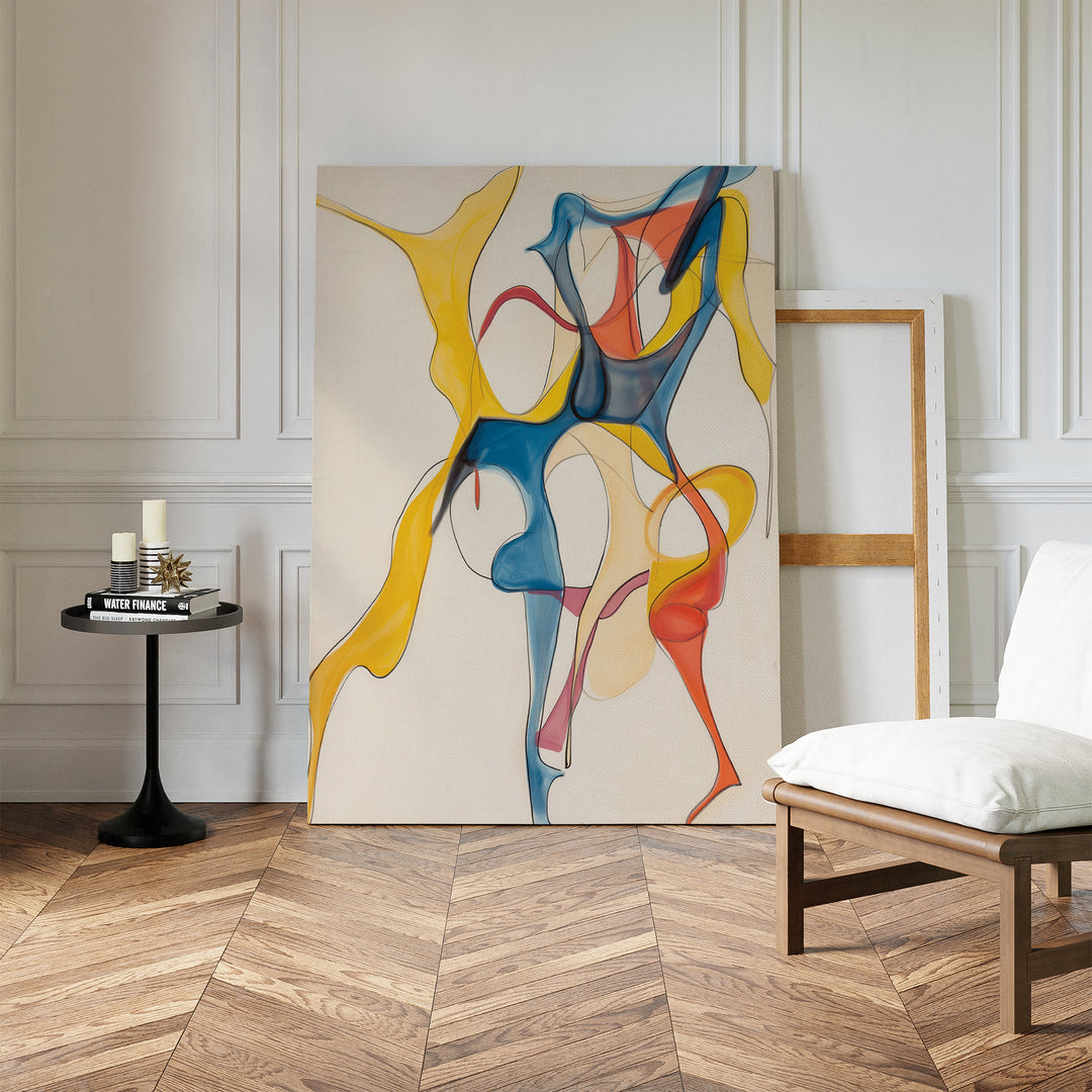 The Dance Of Unity Abstract Canvas Art, featuring flowing yellow, blue, and red shapes, leans against a white paneled wall beside an empty frame, a round table with candles, and a cushioned chair on chevron wood flooring.