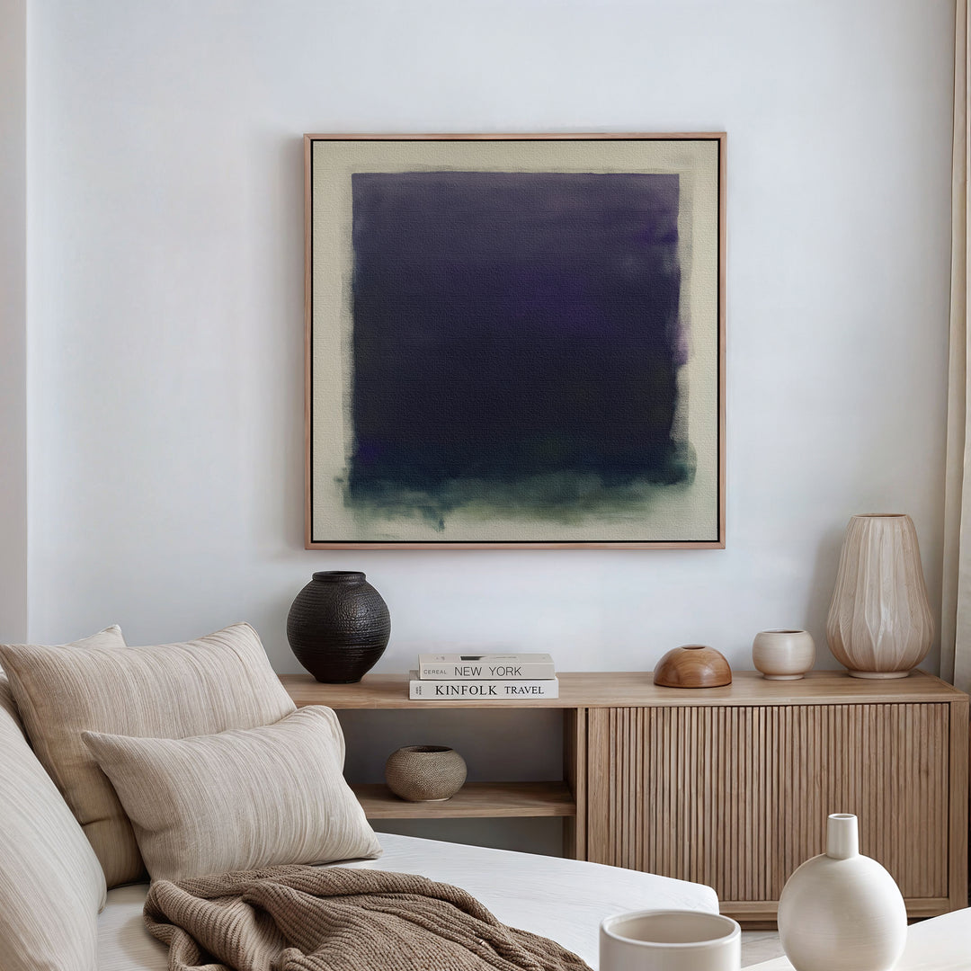 A modern living room features a beige sofa with neutral cushions, a wooden sideboard with books and vases, and the striking Deepest Night Canvas Art in dark blue and green as minimalist wall decor.