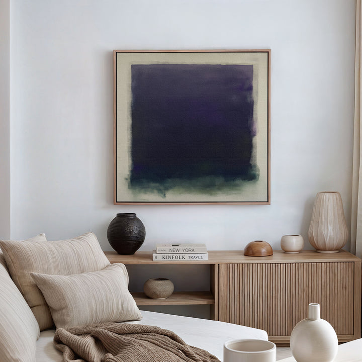 A modern living room features a beige sofa with neutral cushions, a wooden sideboard with books and vases, and the striking Deepest Night Canvas Art in dark blue and green as minimalist wall decor.