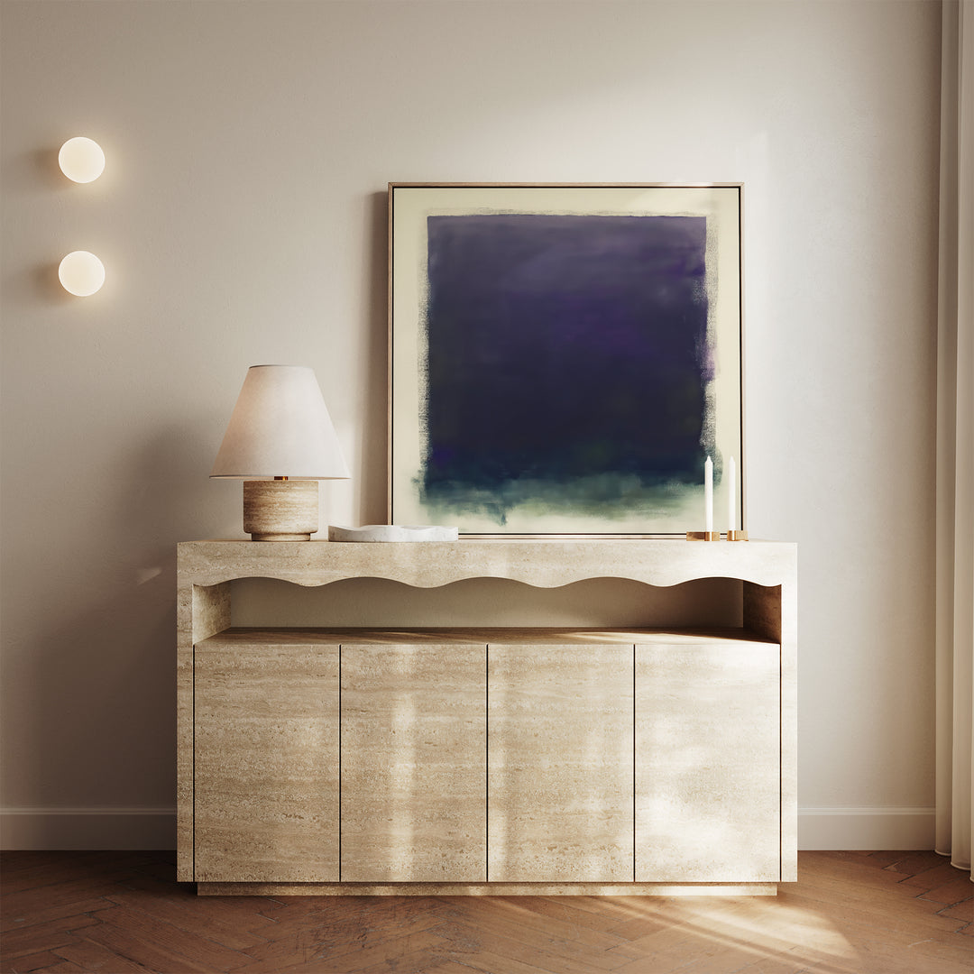 A minimalist console table with a wavy front holds a lamp, two candles, and the Deepest Night Canvas Art in deep blue and green; two round wall lights are on the left, while sunlight filters in from the right.
