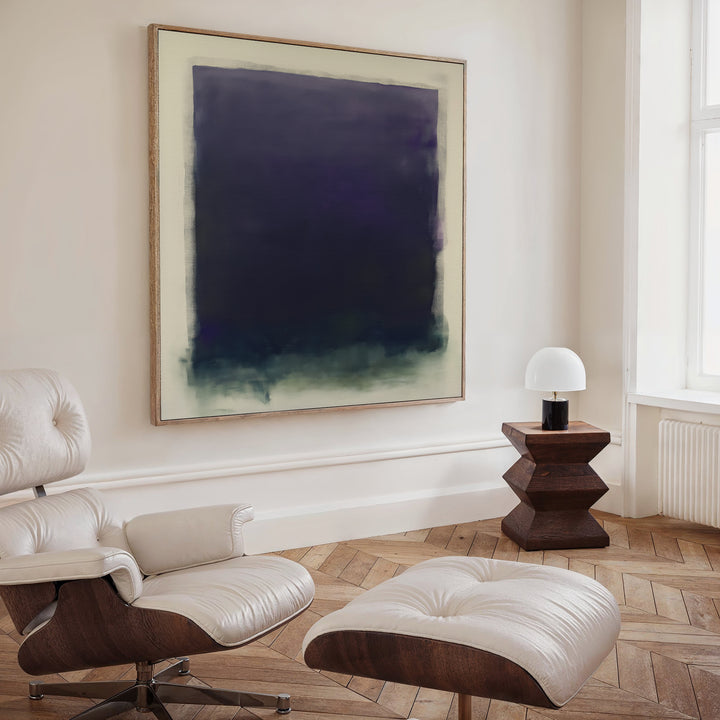 A modern, minimalist room features a white leather lounge chair with ottoman, a wooden side table with a white dome lamp, and the Deepest Night Canvas Art in dark blue and green tones displayed prominently on the wall.