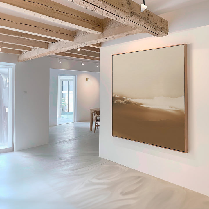 Minimalist interior with light wooden ceiling beams and white walls, featuring the Desert Dusk Abstract Canvas Art in beige and brown. Sunlight highlights modern furniture and open doorways in the background.