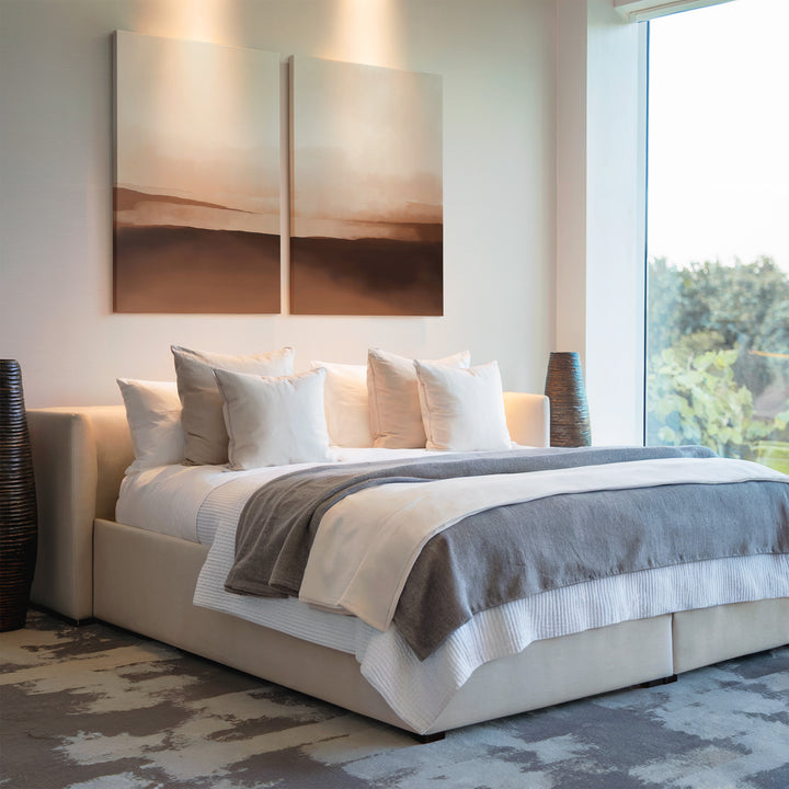 A modern bedroom with a large bed in white and gray bedding, multiple pillows, and the Desert Landscape Set of 2 art above the headboard. Large windows bring in natural light, with decorative vases placed beside the bed.