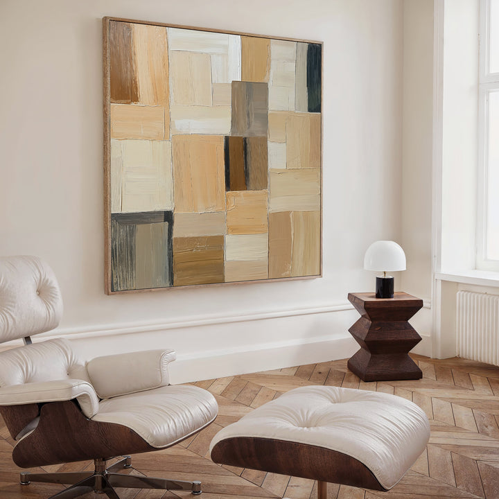 A modern living room with a white leather lounge chair and ottoman, geometric wooden side table with white lamp, Desert Mosaic Abstract Canvas Art on the wall, and light wood herringbone floors.