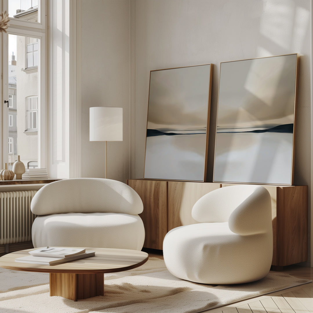 A modern living room features the Desert Quietude Set of 2 white curved armchairs, a low wooden coffee table, and a sideboard with minimalist wall art. Large windows fill the space with natural light, creating a bright, airy atmosphere.
