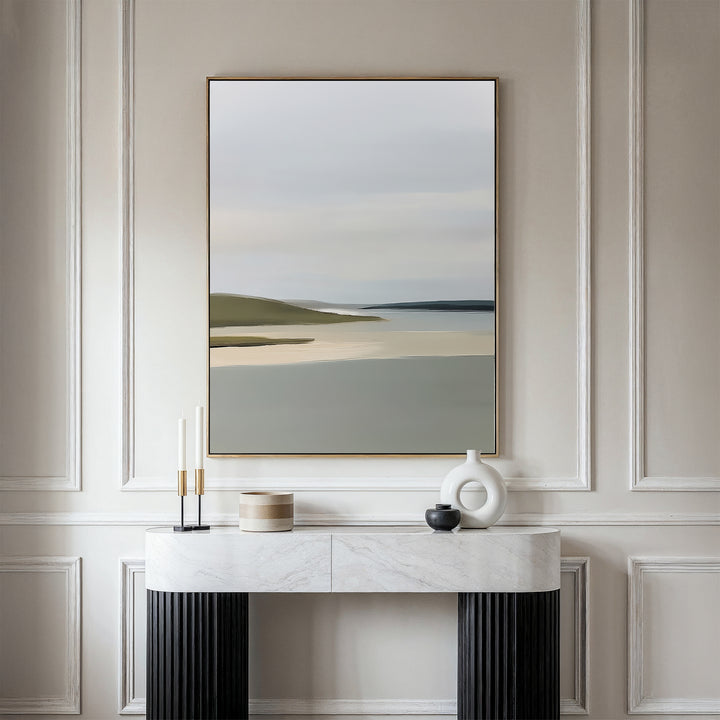 A minimalist console table with decor stands against an elegant, light-paneled wall. Above it hangs the Distant Shores Canvas Art, showcasing a serene landscape of soft water and rolling hills for a touch of nature-inspired style.