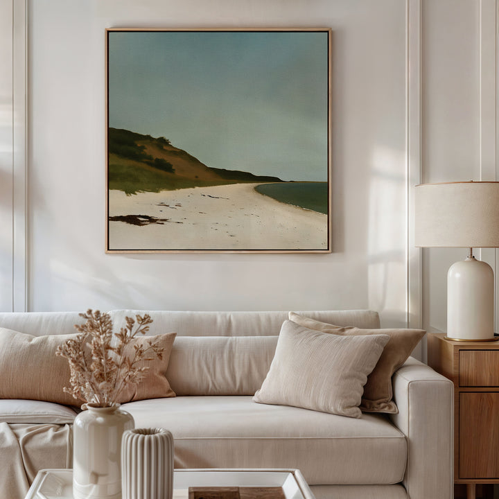 A modern living room features a beige sofa with light cushions, a side table with a lamp, and a vase of dried flowers. The Drift Shore Canvas Art hangs above the sofa, bringing elegant coastal style to the space.