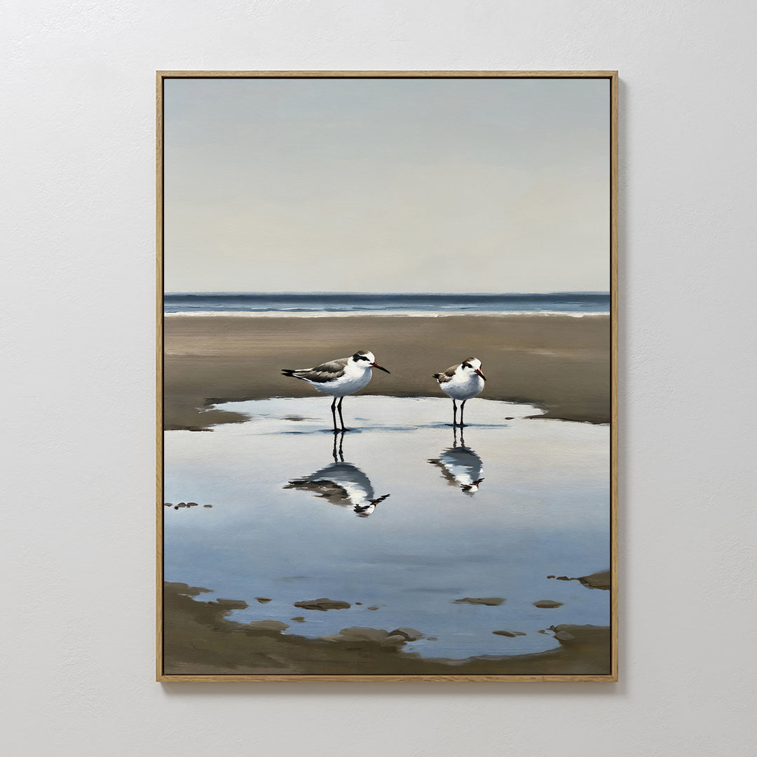 The Drifted Calm Canvas Art features two shorebirds by a reflective pool on a sandy beach with ocean and sky beyond—perfect minimalist wall art to bring a serene coastal vibe to any interior.
