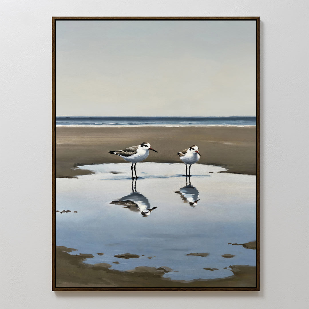 Drifted Calm Canvas Art: A framed painting of two shorebirds wading in a shallow pool on a sandy beach, with their reflections and a peaceful ocean backdrop—perfect minimalist wall art for coastal interiors.