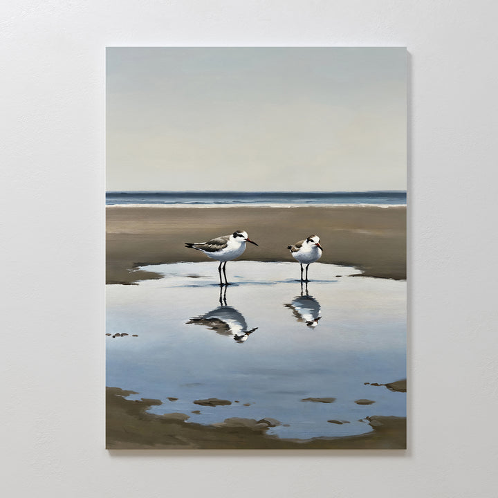 Drifted Calm Canvas Art features two shorebirds by a shallow pool on a sandy beach, their reflections captured against a soft ocean and sky—an ideal minimalist piece to add serene beauty to contemporary interiors.