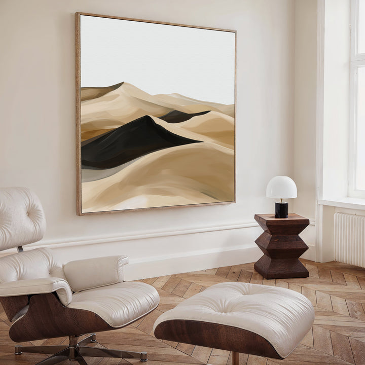 A modern living room features a white leather lounge chair and ottoman, a geometric wooden side table with a white lamp, and Dune Waves Abstract Canvas Art on the wall. Light wood floors and a large window enhance the contemporary decor.