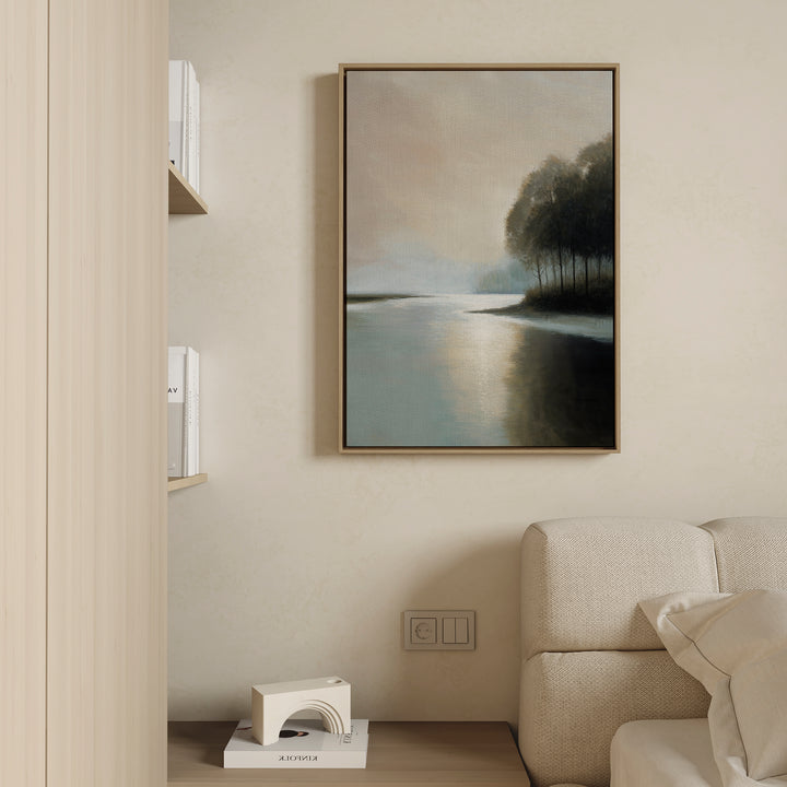 A minimalist living room corner features a beige sofa, calming decor, a small shelf with books and a sculptural white object, and the Dusklake Canvas Art landscape painting of a lake with trees hanging on a light wall.