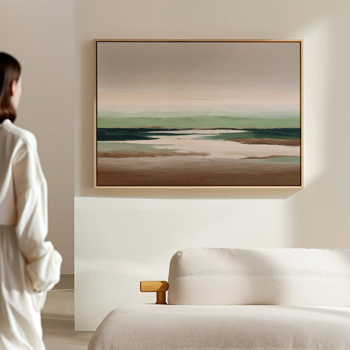 A person stands in a minimalist room, admiring the Earthbound Horizon Canvas Art—a striking abstract landscape with earthy tones and soft greens—displayed above a light-colored textured sofa.