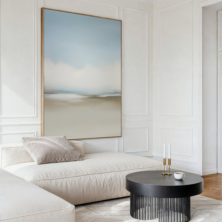 A modern living room features a cream sofa, a gray round coffee table with two candlesticks and a cup, and the Faded Silence Canvas Art in soft blue and beige tones as minimalist wall decor above the seating area.