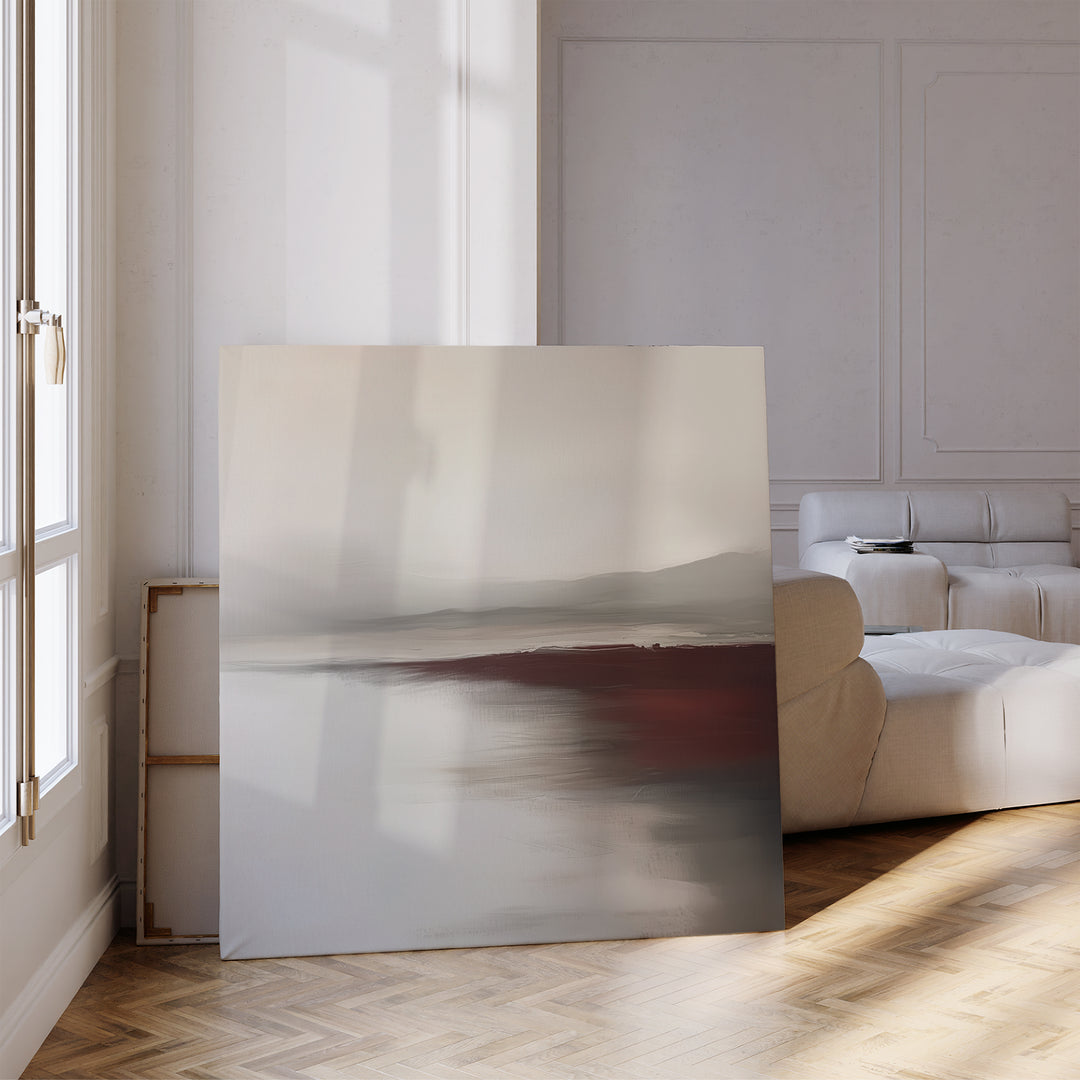 The Fading Light Canvas Art, featuring muted gray, beige, and maroon tones, leans against a wall in a bright minimalist living room with parquet flooring, white walls, and a cream-colored sofa.