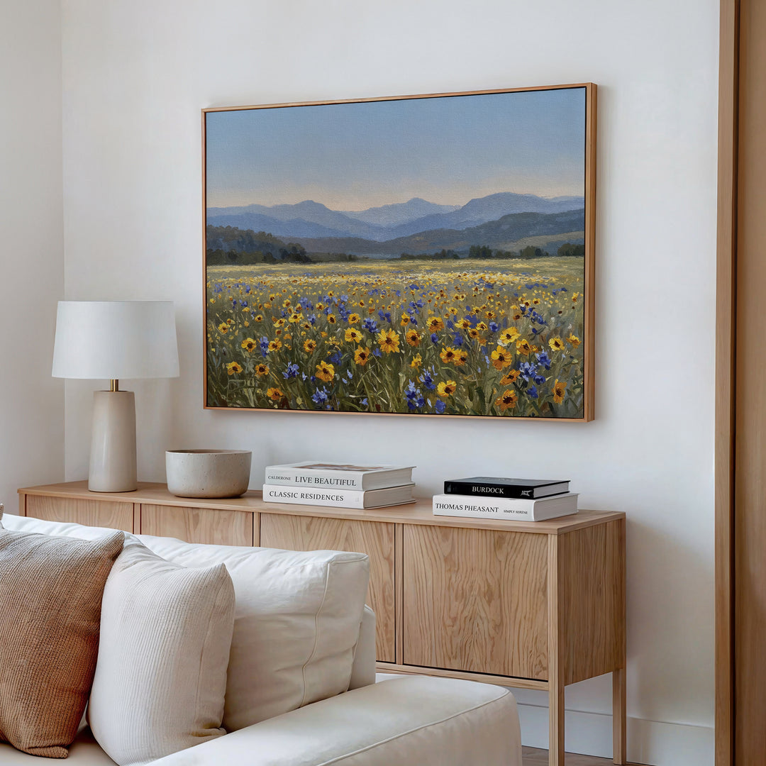 A cozy living room with a wooden sideboard, books, a lamp, and a bowl features modern decor and the Fields of Color Canvas Art wall print above a cream-colored sofa adorned with plush cushions.