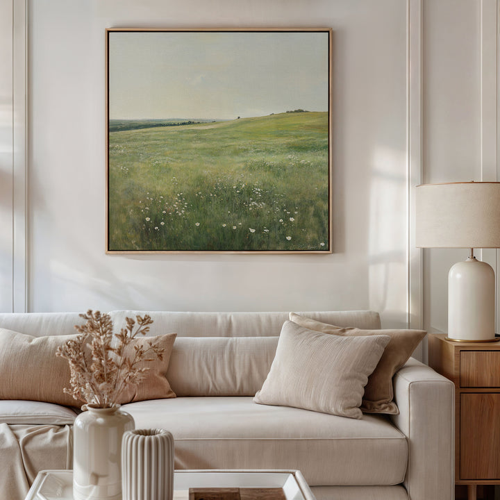 A bright living room features a beige sofa with neutral pillows, a wooden side table and white lamp. Above the couch hangs the Floral Meadow Canvas Art, and dried flowers in a vase sit on the coffee table for cozy decor.