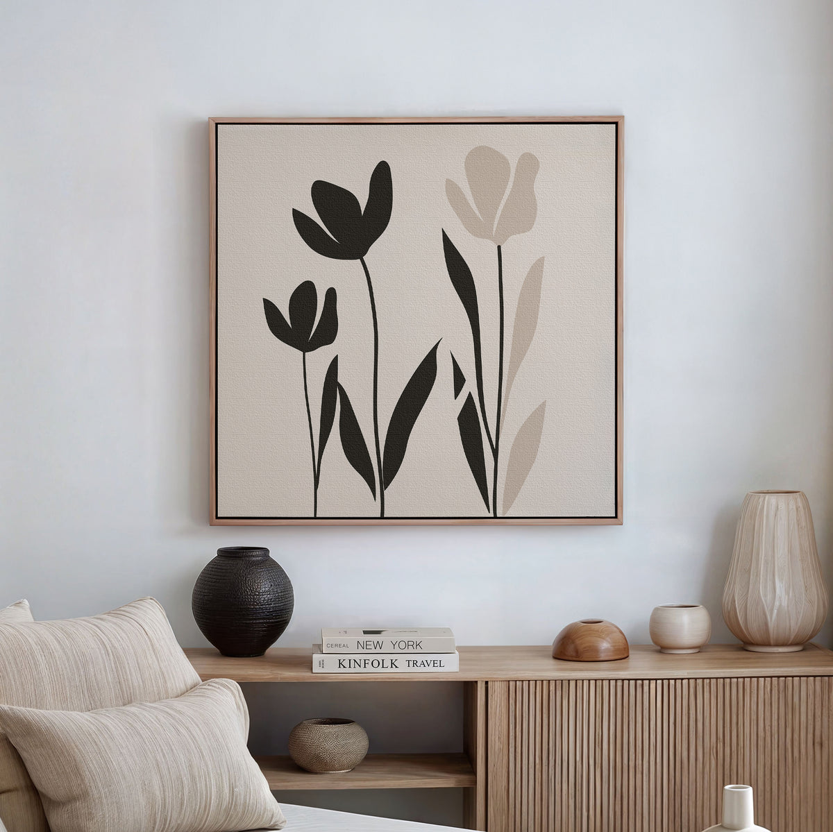 A minimalist living room features a wooden sideboard, neutral decor, and the Floral Simplicity Canvas Art—a framed print with three black and beige tulip-like flowers—adding elegant wall art above a crisp white wall.