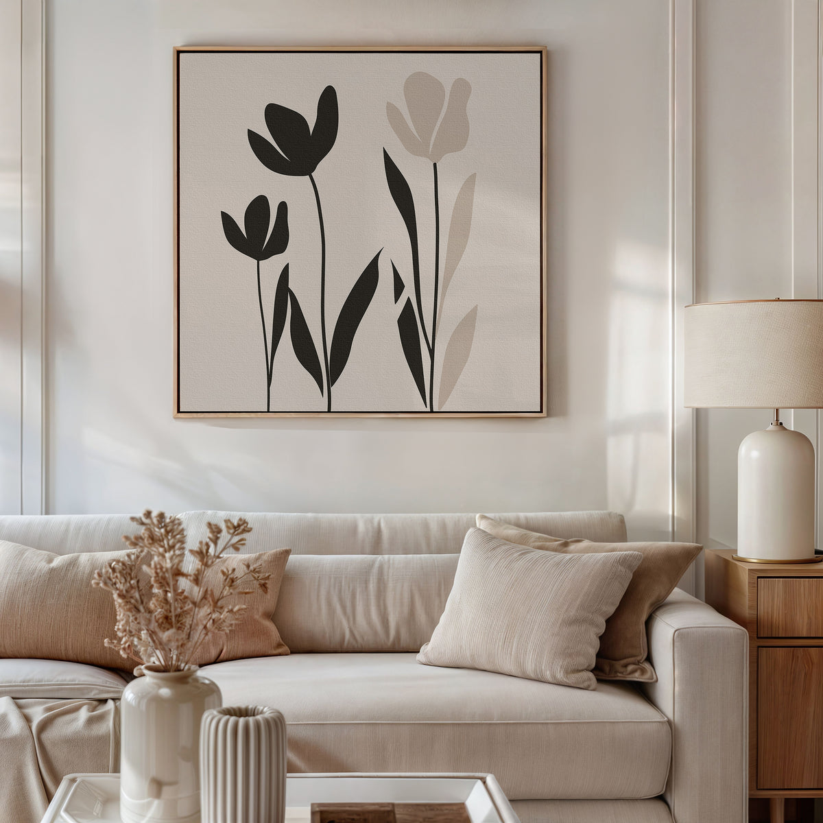 A neutral-toned living room features a beige sofa, light cushions, dried flowers in a vase, a table lamp, and the Floral Simplicity Canvas Art—minimalist black and beige wall art—hanging above the sofa.