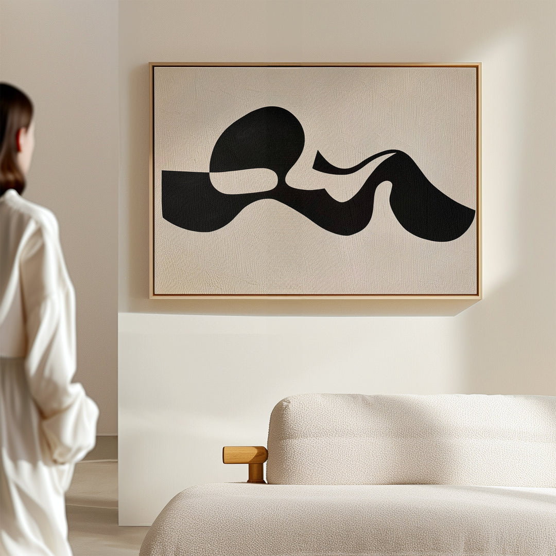 A person in white stands in a minimal, modern room with a cream sofa. Sunlight casts soft shadows across the walls, highlighting the Fluid Forms Abstract Canvas Art displayed prominently above the furniture.