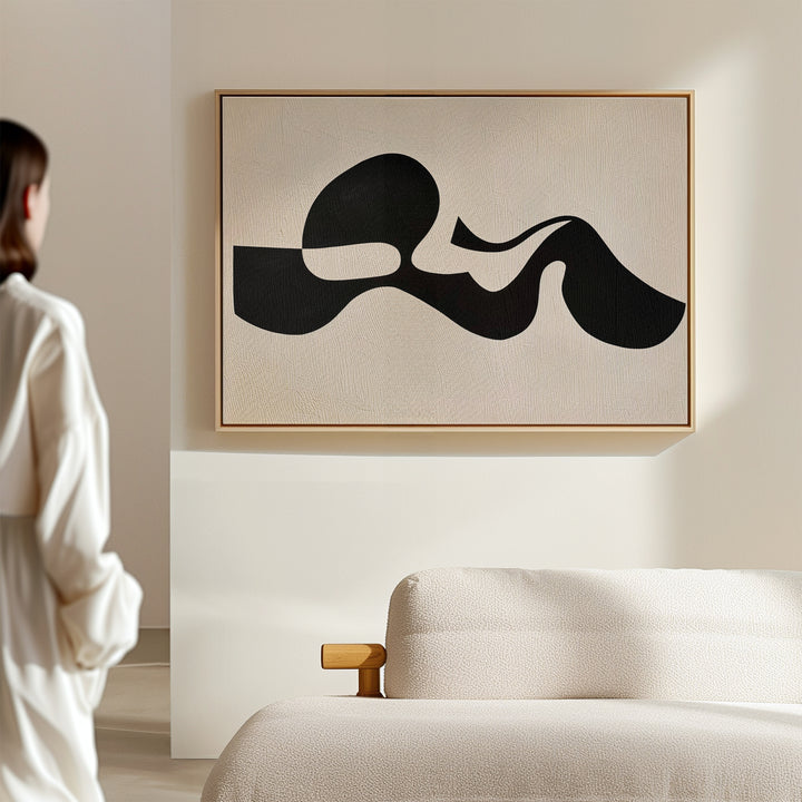 A person in white stands in a minimal, modern room with a cream sofa. Sunlight casts soft shadows across the walls, highlighting the Fluid Forms Abstract Canvas Art displayed prominently above the furniture.
