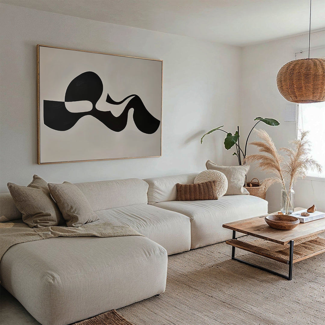 A modern living room with a beige sectional sofa, neutral pillows, wooden coffee table, Fluid Forms Abstract Canvas Art in black and white, woven pendant light, pampas grass in a vase, and a leafy potted plant by the window.
