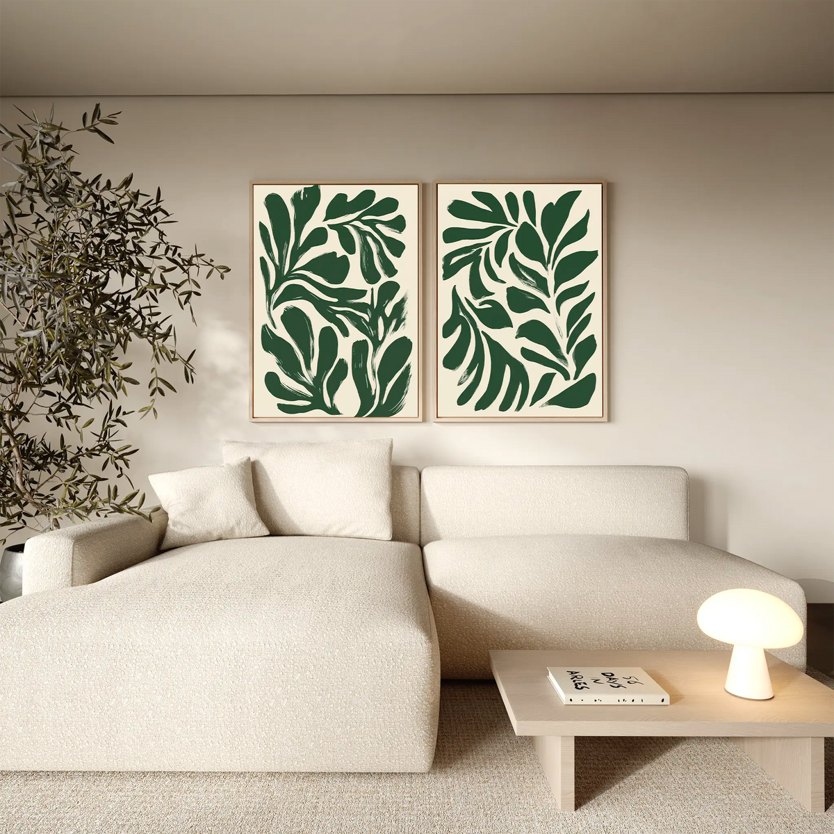 A modern living room with a light beige sofa, a wooden coffee table with a small lamp, a potted plant, and the Forest Leaves Set of 2 framed botanical wall art prints of abstract green leaves hanging above the sofa.