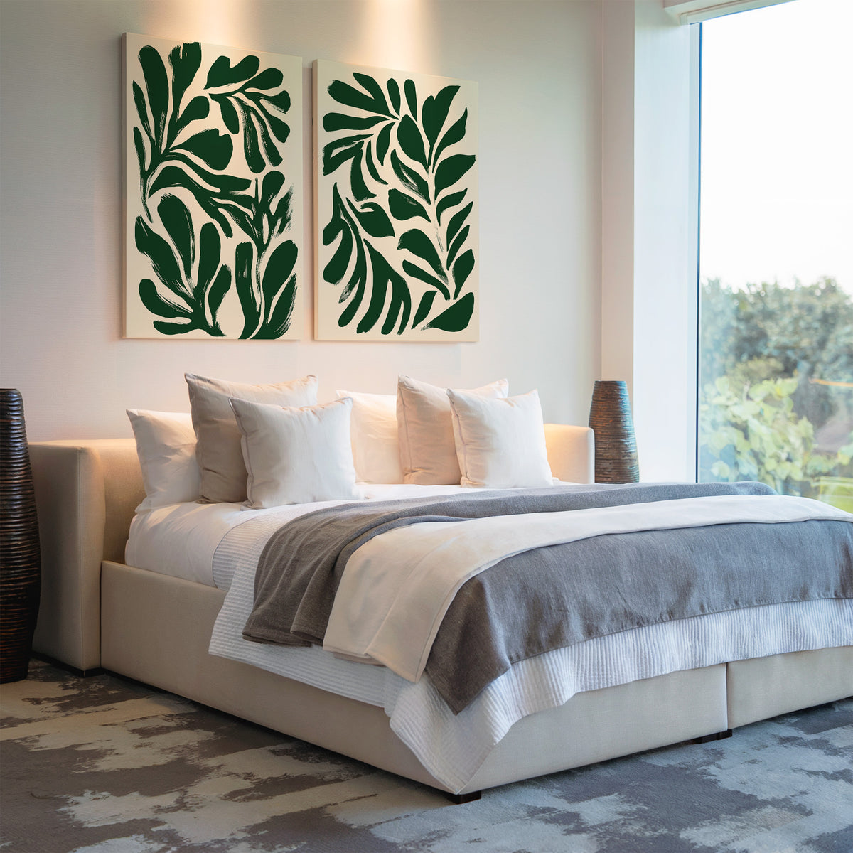 A modern bedroom features a large bed with white and gray bedding, multiple white pillows, and the Forest Leaves Set of 2 botanical wall art above the headboard. Woven vases flank the bed, while a large window offers views of greenery.
