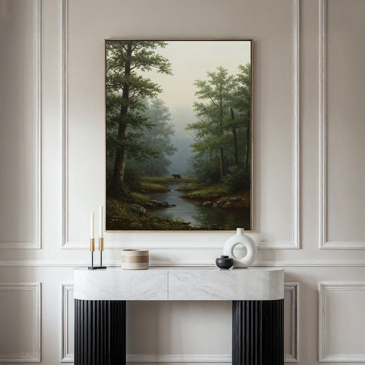 The Forest Passage Canvas Art, depicting a forest with a stream and distant black bear, is displayed on a cream wall above a modern marble console adorned with candles and neutral-toned vases.