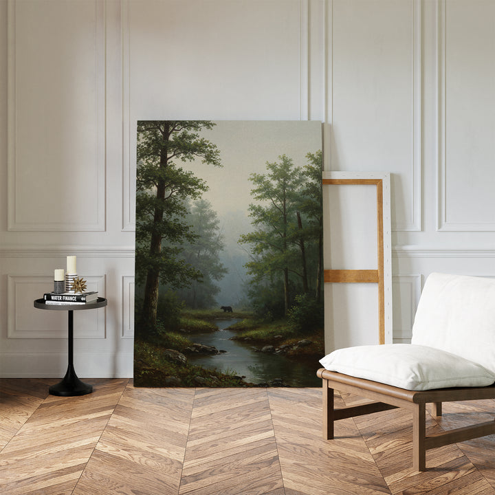The Forest Passage Canvas Art, a large landscape print of a forest and stream, leans against a white-paneled wall in a minimalist room with a cushioned chair, round table, and herringbone floor—perfect for forest decor enthusiasts.