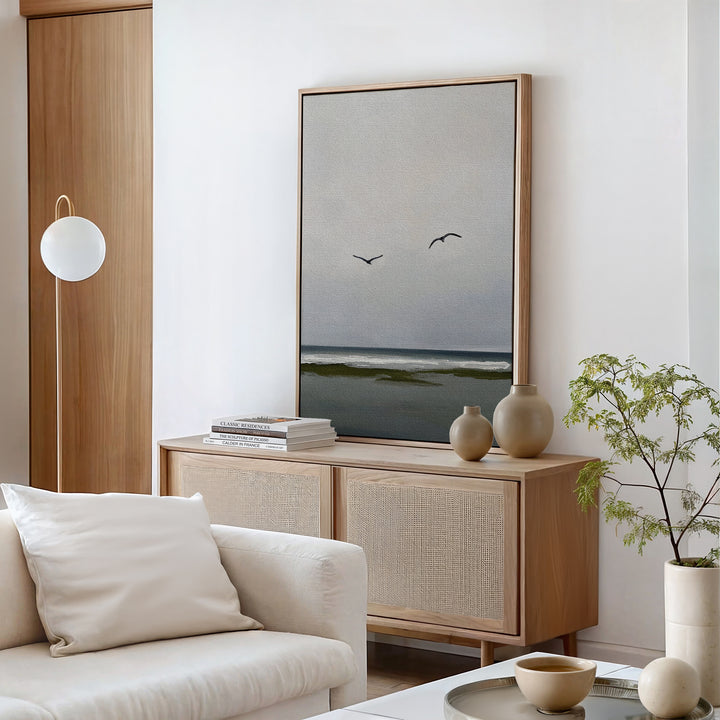 Minimalist living room with a light wood sideboard, neutral vases, small plant, and the Freeflight Canvas Art—an ocean scene with two birds. A white armchair, round coffee table, and modern lamp complete the serene decor.