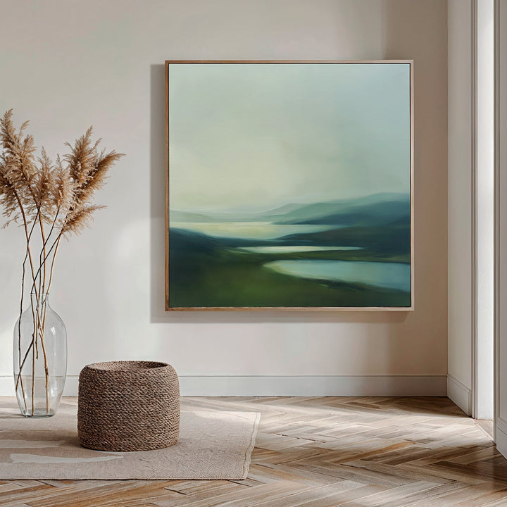 A minimalist room with wooden parquet flooring, a woven ottoman, and a clear glass vase of pampas grass is bathed in natural light, featuring Gentle Valleys Abstract Canvas Art—perfect for refined living room decor.